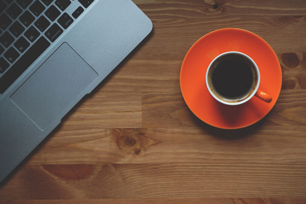 Overhead view of a laptop and a cup of coffee on a wood surface