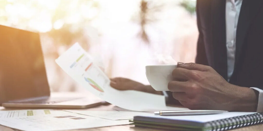 Person drinking coffee and reviewing paperwork